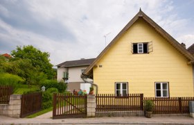 Ein gelbes Haus mit Spitzdach und Holzzaun in einer l&auml;ndlichen Umgebung.