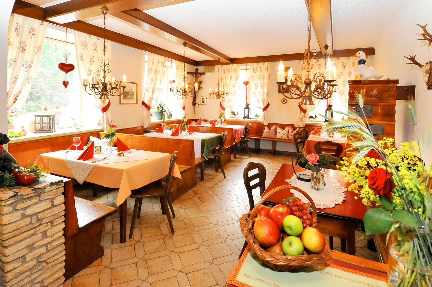 Gemütlicher Restaurantbereich mit Holzmöbeln, dekorativen Vorhängen und Blumenarrangements.