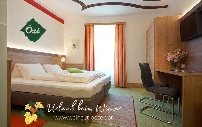 Gem&uuml;tliches G&auml;stezimmer mit Doppelbett, Schreibtisch und Stuhl, dekoriert mit Blumen. Helle Vorh&auml;nge und Teppichboden.