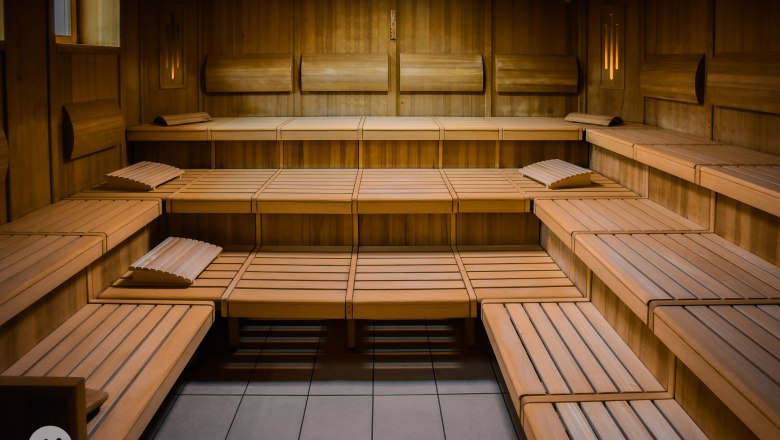 Innenansicht einer leeren Holzsauna mit mehreren Sitzreihen und Kopfstützen.