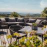 Terrasse mit Sitzm&ouml;beln und Pflanzen, im Hintergrund eine weite Landschaft.