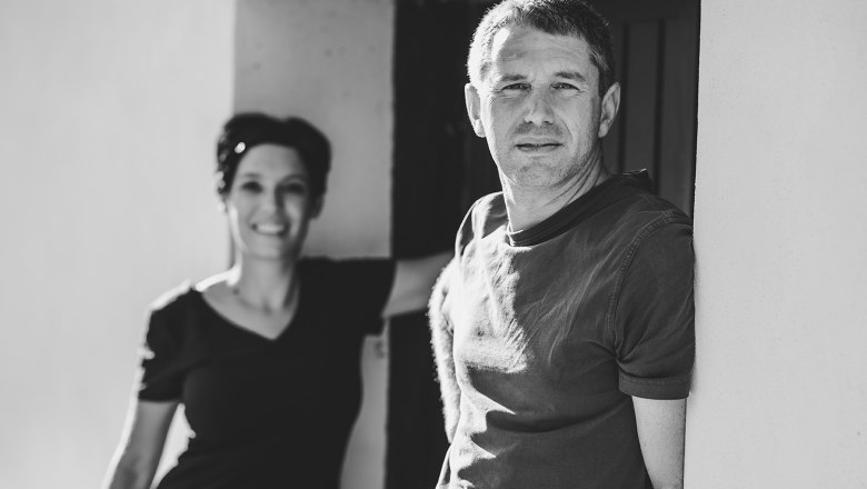 Schwarz-wei&szlig; Foto von zwei Personen mit Weinflaschen vor einer T&uuml;r.