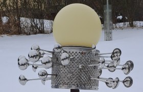 Eine Skulptur im Schnee mit einer kugelf&ouml;rmigen Lampe und metallischen Elementen.