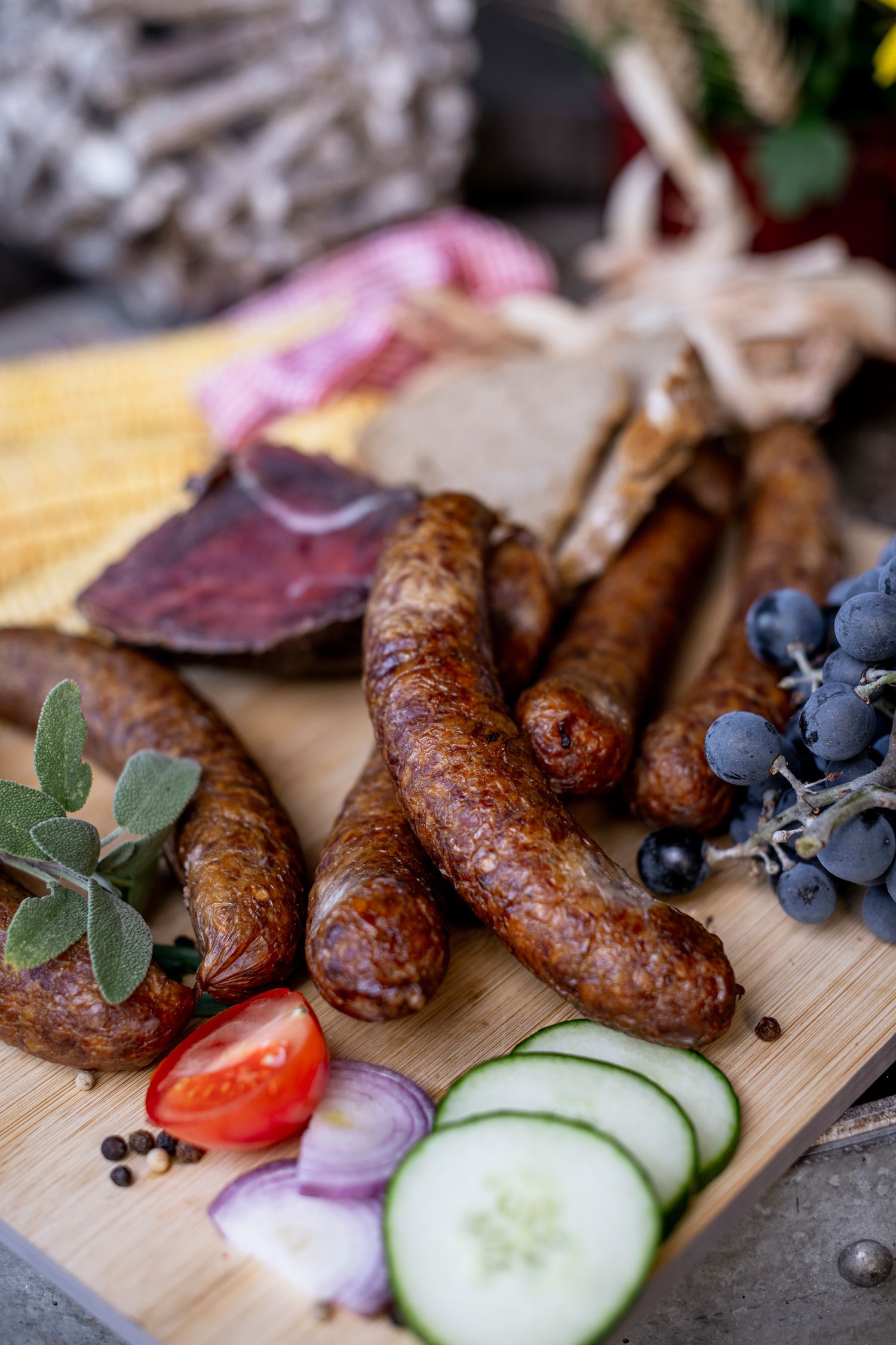 Nahaufnahme von Würsten, Trauben, Tomaten, Gurken und Zwiebeln auf einem Holzbrett.