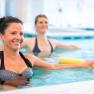 Zwei Frauen machen Wassergymnastik in einem Pool mit gelben Schwimmnudeln.