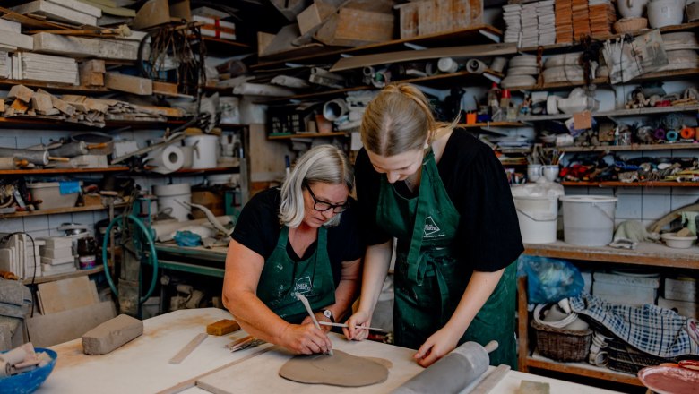 Zwei Frauen arbeiten in einer Keramikwerkstatt an einem Tonst&uuml;ck.