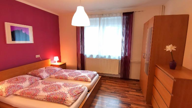 Gem&uuml;tliches Schlafzimmer mit Doppelbett, pinker Wand und Holzm&ouml;beln.