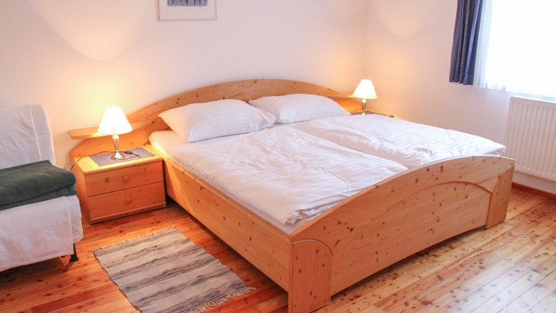 Gemütliches Schlafzimmer mit Doppelbett, Holzboden und Nachttischen mit Lampen.