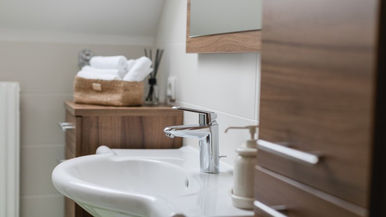 Modernes Badezimmer mit Waschbecken, Holzschränken und Handtüchern in einem Korb.