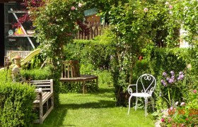 Ein idyllischer Garten mit B&auml;nken, einem wei&szlig;en Stuhl und bl&uuml;henden Pflanzen.