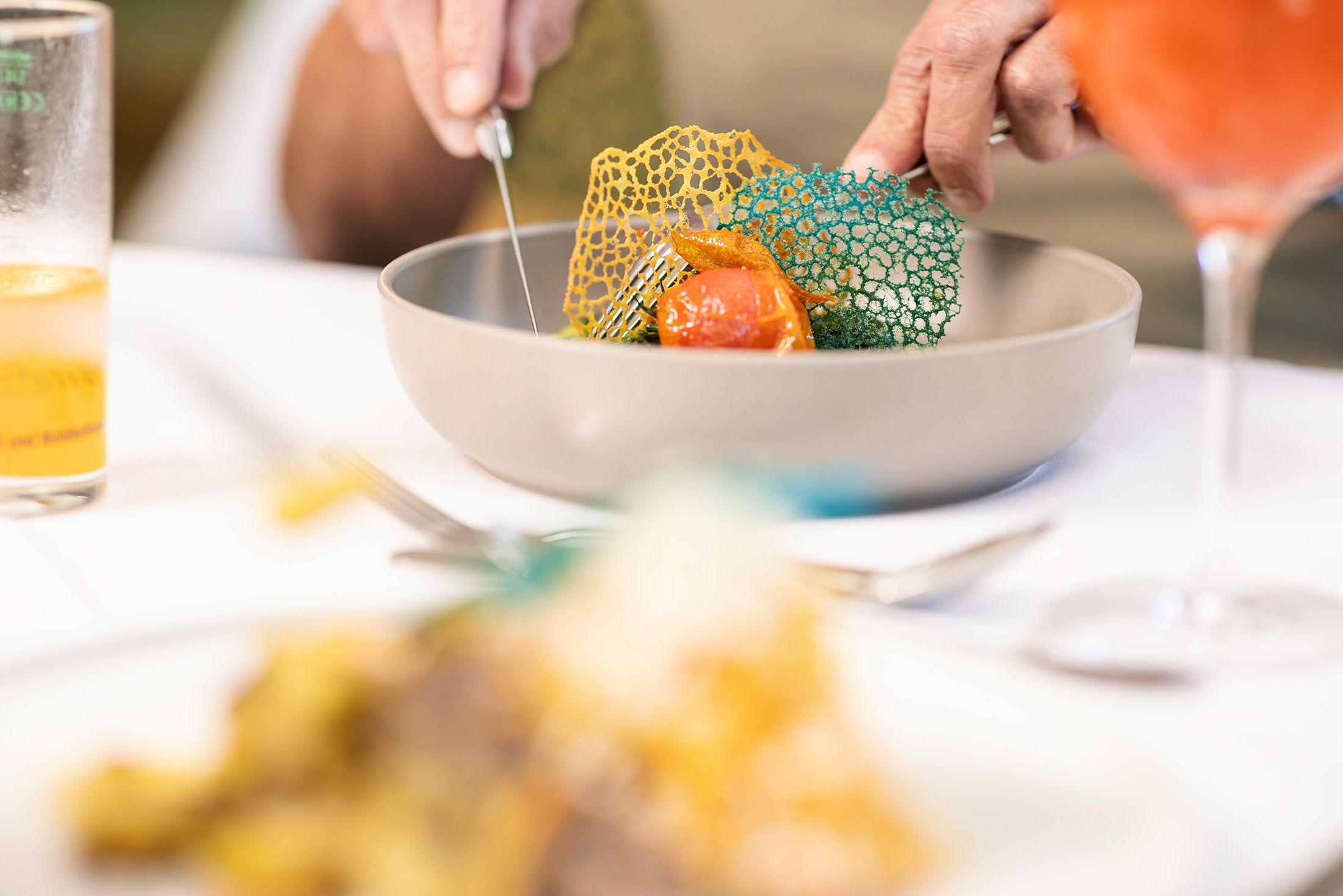 „Im Restaurant Kreuzberg wird einem Gast am gedeckten Tisch ein frisch zubereitetes Gericht serviert. Auf dem Tisch stehen Getränke und Speisen. Die helle, freundliche Atmosphäre vermittelt einen Einblick in den Restaurantbesuch und den persönlichen Service.“