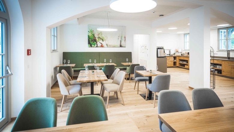 Modernes Restaurant mit Holztischen und gepolsterten St&uuml;hlen, helle Beleuchtung und Kunst an der Wand.