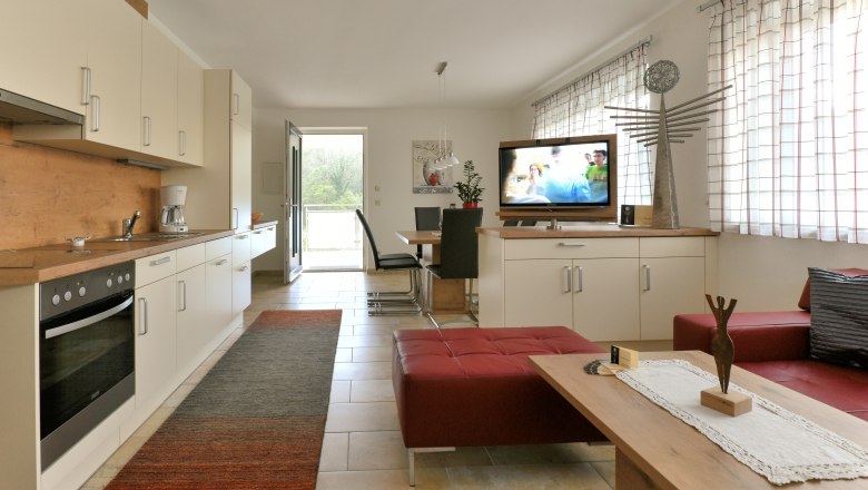 Moderne Wohnk&uuml;che mit Einbauk&uuml;che, Esstisch, Fernseher und roten Sitzm&ouml;beln.