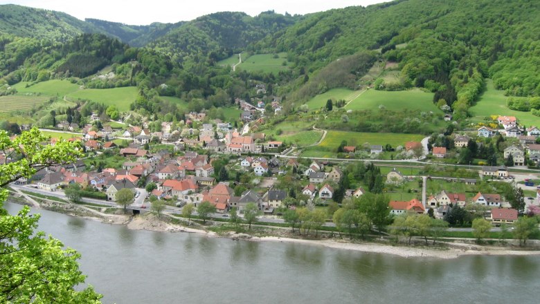 Luftaufnahme von Aggsbach mit Fluss und gr&uuml;nen H&uuml;geln im Hintergrund.