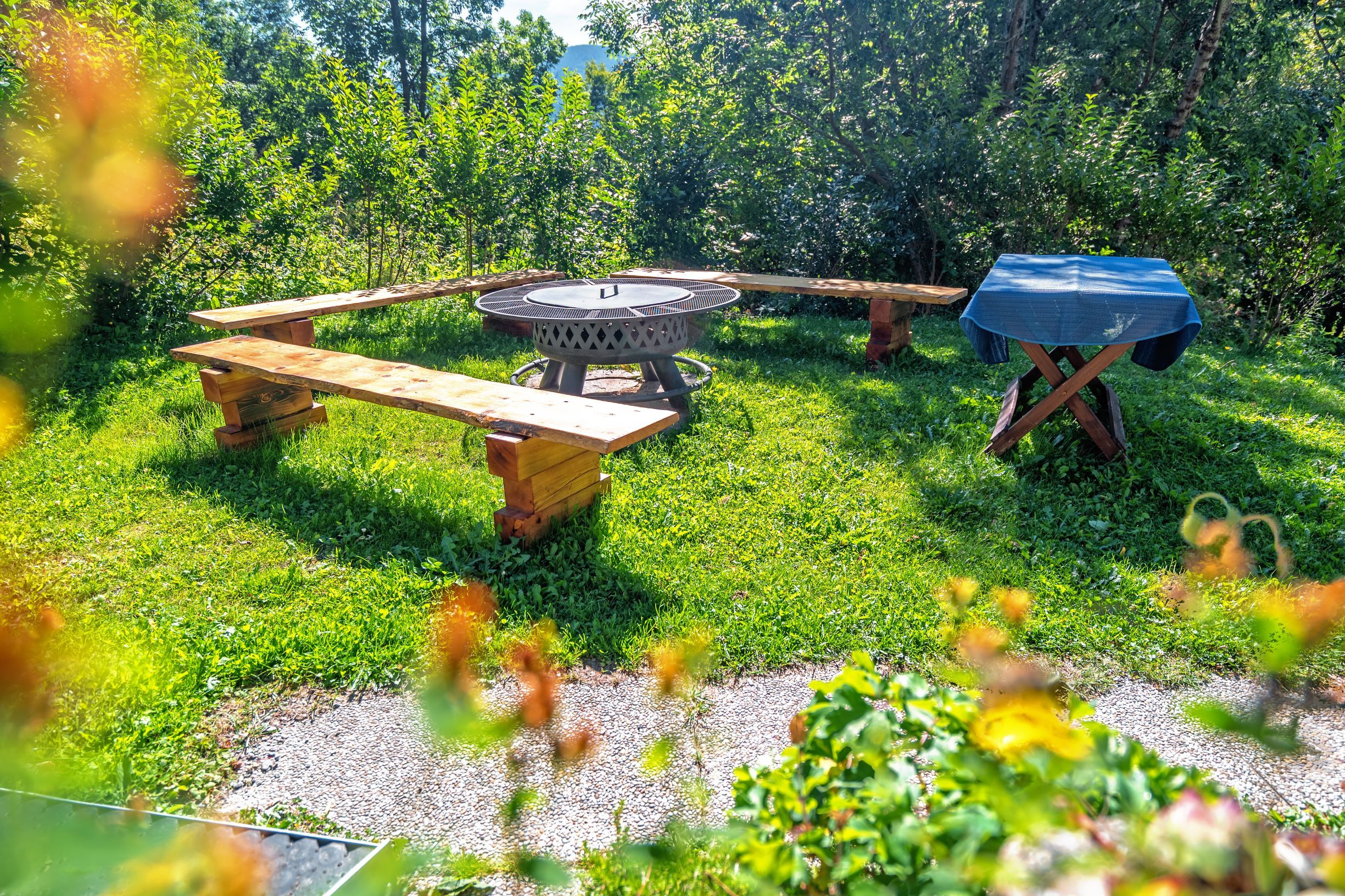 Ein Grillplatz mit Holzbänken und einem Tisch im Freien, umgeben von grüner Vegetation.