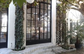 Eingangsbereich mit gro&szlig;en Glasfenstern, Efeu und Pflastersteinen.