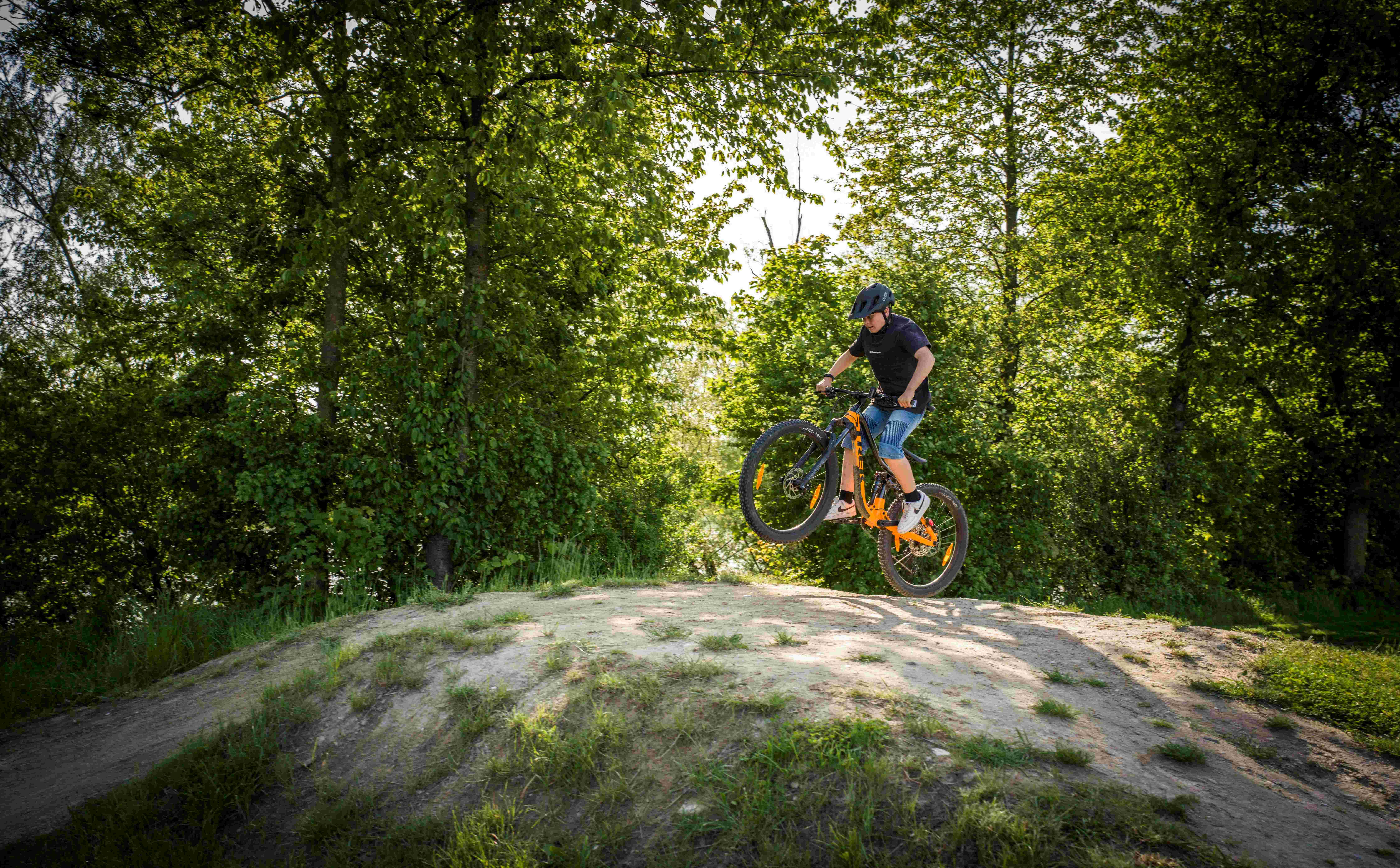Ein Mountainbiker springt mit seinem Fahrrad über einen Hügel in einem bewaldeten Gebiet.