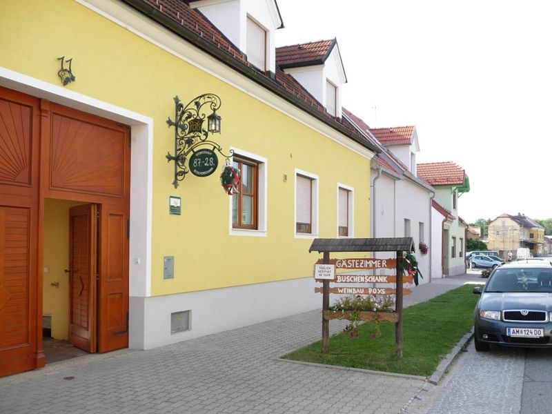 Gelbes Gebäude mit Schild 'Gästezimmer Buschenschank Weinbau Poys' und geparktem Auto davor.