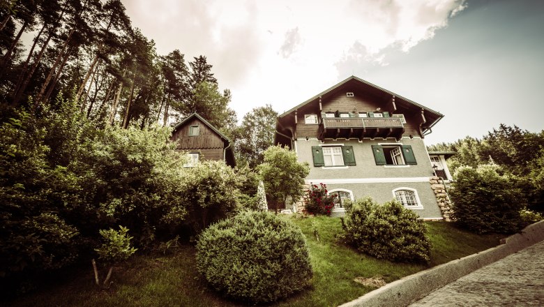 Eine Villa mit gr&uuml;nem Garten und B&auml;umen im Hintergrund.