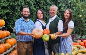 Vier Personen halten K&uuml;rbisse in einem Garten mit vielen K&uuml;rbissen.