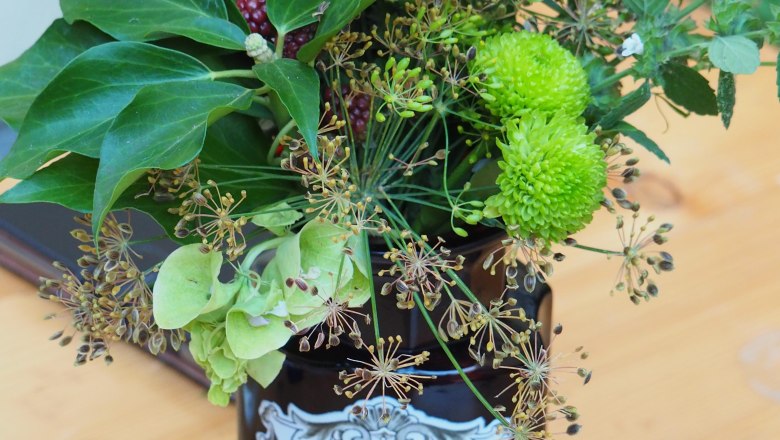 Ein Apothekengef&auml;&szlig; mit der Aufschrift 'RAD. RHEI PULV.' gef&uuml;llt mit Blumen und Beeren auf einem Holztisch.