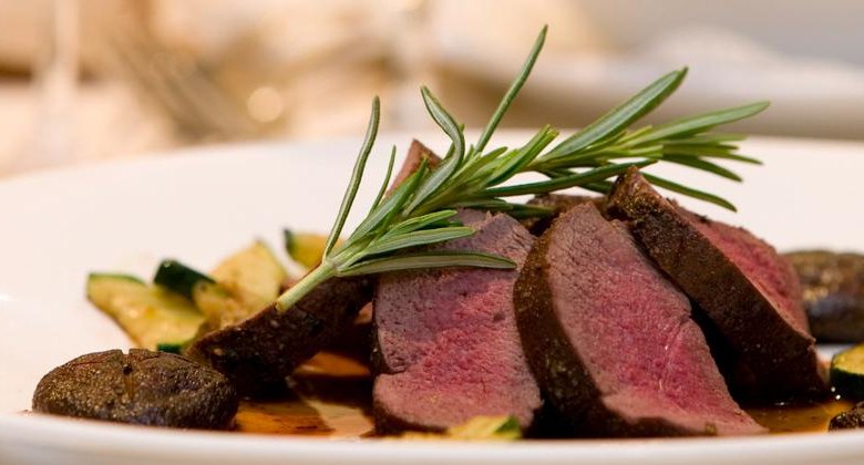 Ein Gourmet-Gericht mit rosa gebratenem Fleisch, garniert mit Rosmarin, auf einem Teller mit Zucchini und Pilzen.