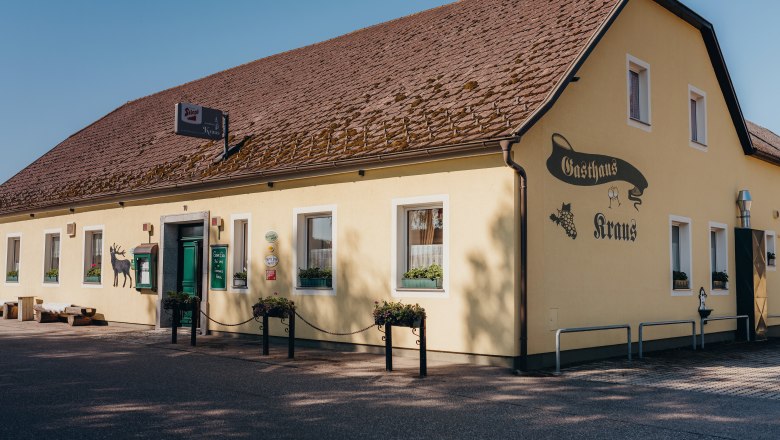 Gelbes Gasthaus mit braunem Dach und gr&uuml;ner T&uuml;r, beschriftet mit 'Gasthaus Kraus'.