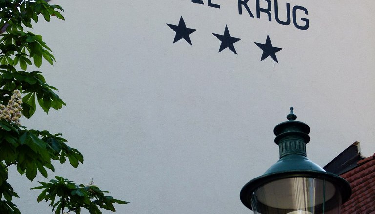 Fassade des Hotel Krug mit drei Sternen, Baum und Stra&szlig;enlaterne.