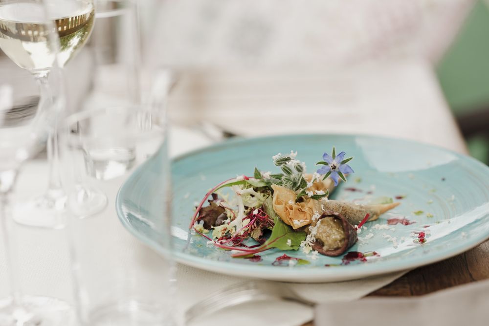 Ein Teller mit Blunzenspitz, Melanzani-Kaviar und Pflücksalat, dekoriert mit essbaren Blüten.