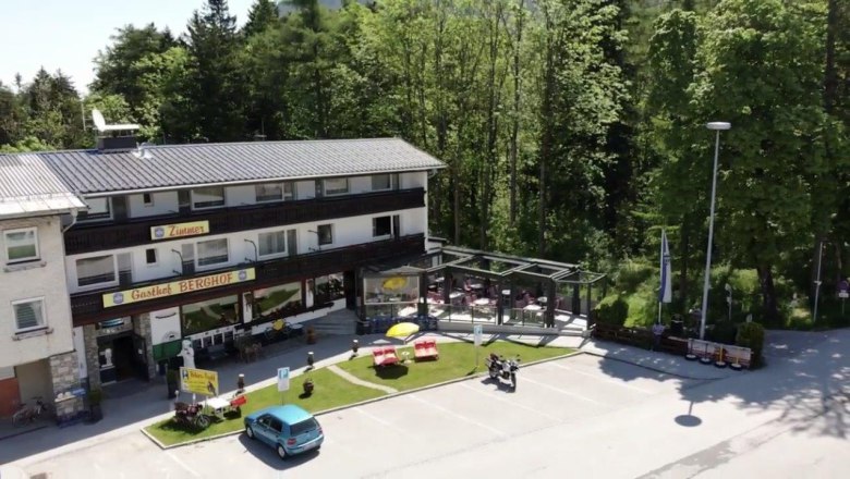 Gasthof Berghof, © Gasthof Berghof Außenansicht des Gasthofs Berghof mit Terrasse und Parkplatz, umgeben von Bäumen.