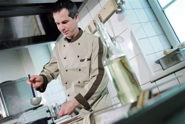 Ein Koch in einer professionellen Küche schöpft mit einer Kelle aus einem Topf.