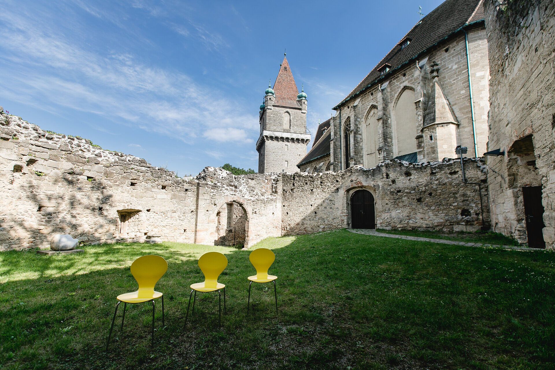 Die Ruinen der Burg Perchtoldsdorf strahlen eine geheimnisvolle Atmosphäre aus, während die sanften Hügel des Wienerwaldes im Hintergrund leuchten. Gelbe Stühle laden dazu ein, die Schönheit der Umgebung zu genießen und die Seele baumeln zu lassen. Hier, wo Geschichte und Natur aufeinandertreffen, wird jeder Besuch zu einem unvergesslichen Erlebnis.