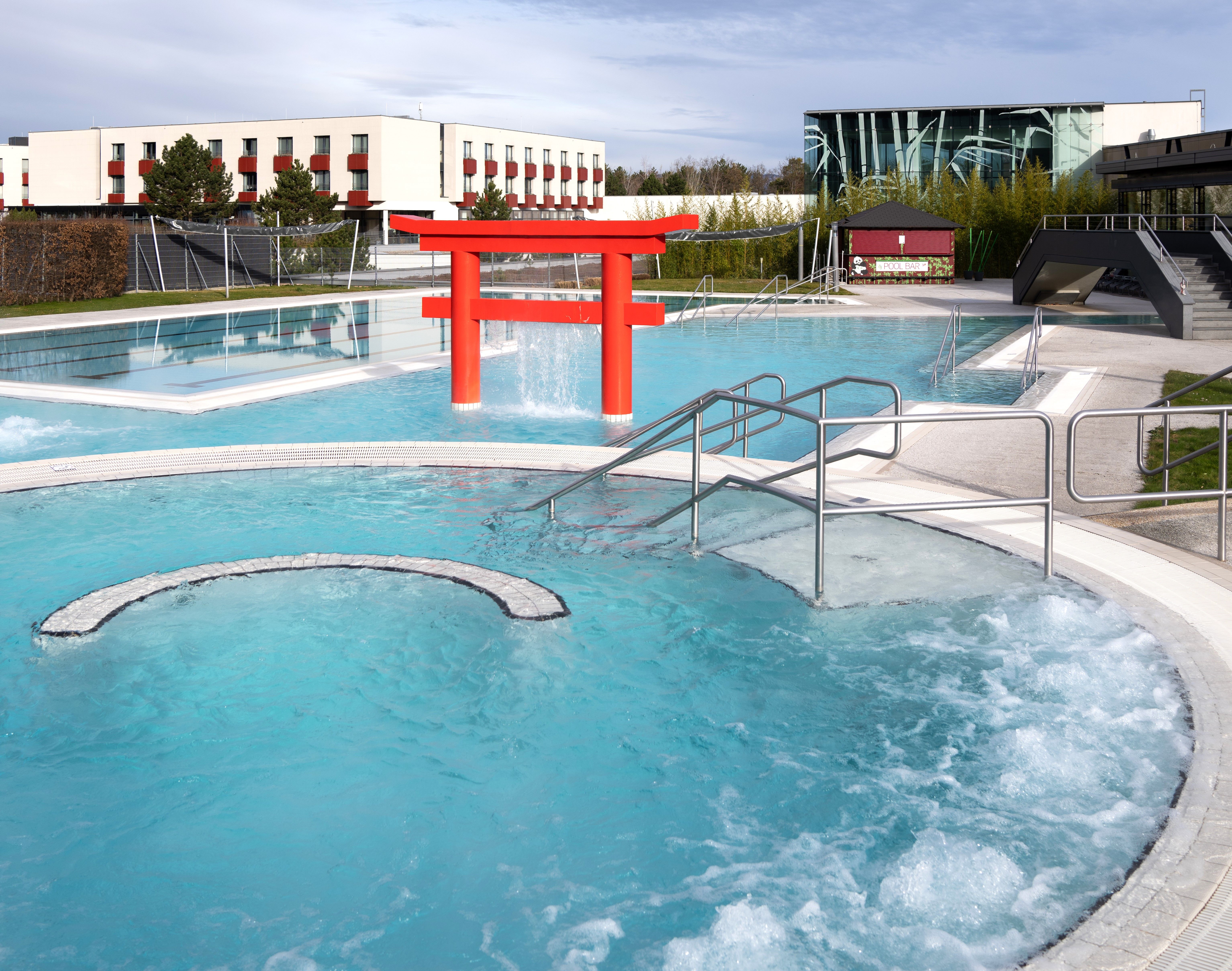 Außenpool des Hotel Linsberg Asia mit rotem Torii und modernen Gebäuden im Hintergrund.