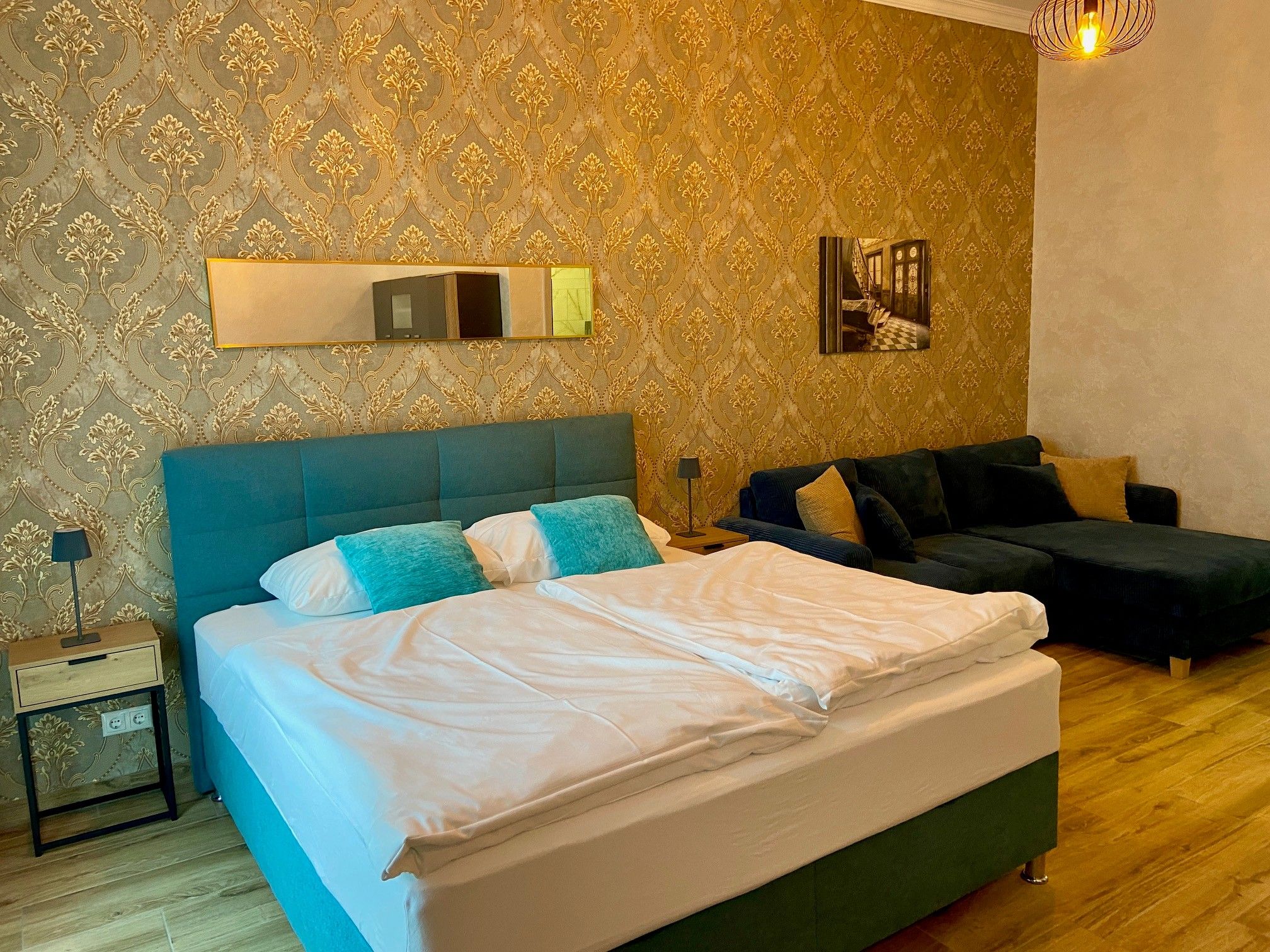 Elegantes Hotelzimmer mit Doppelbett, blauer Couch und goldener Tapete.