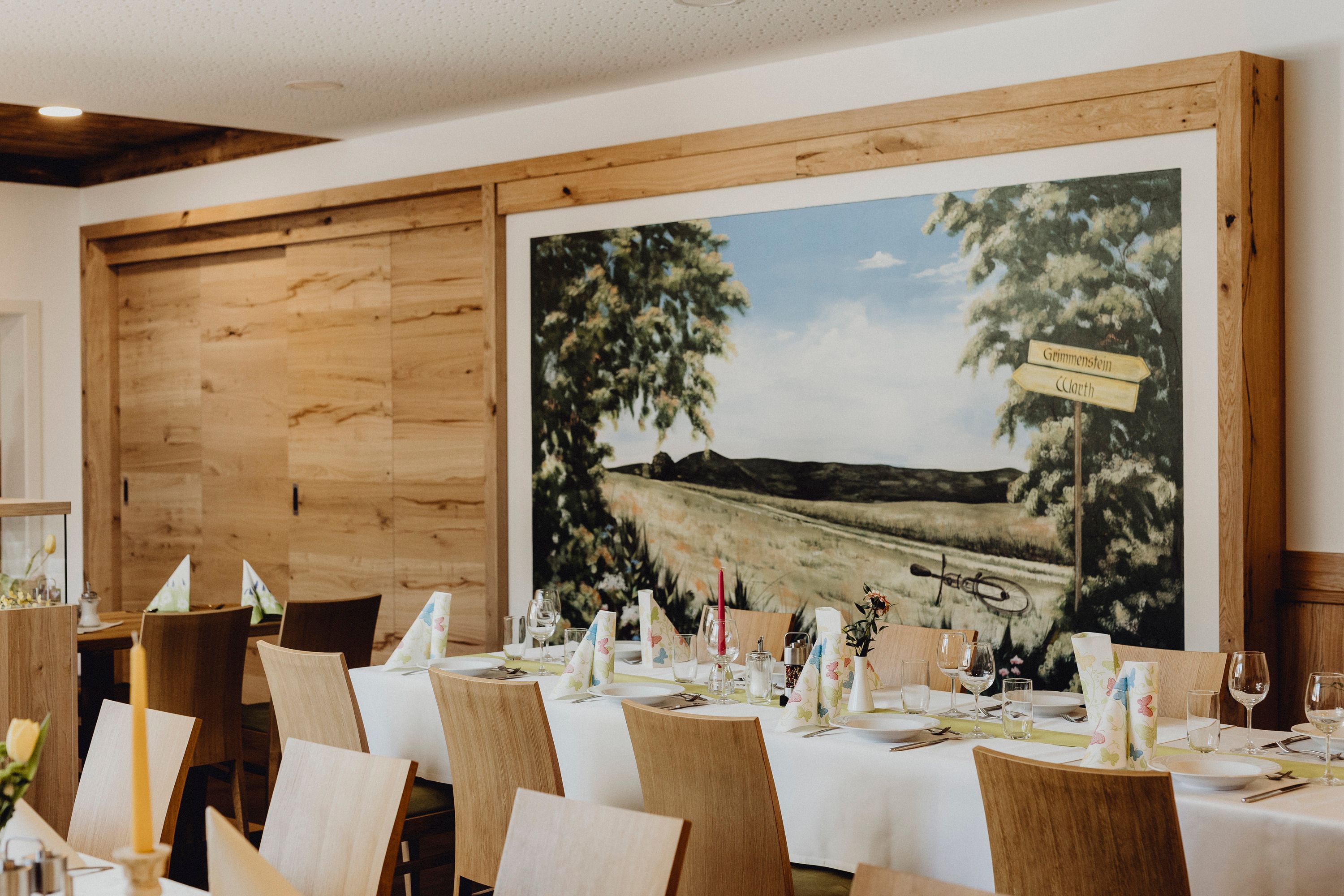 Innenansicht eines Wirtshauses mit gedecktem Tisch und Wandgemälde.