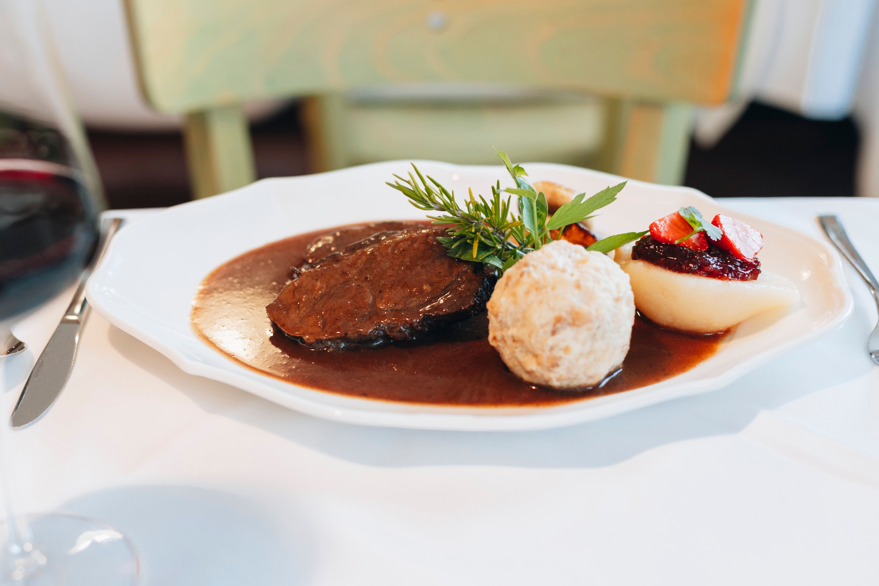 Ein Teller mit Hirschrücken, Semmelknödel, Birne mit Preiselbeeren und Soße, dekoriert mit Kräutern.