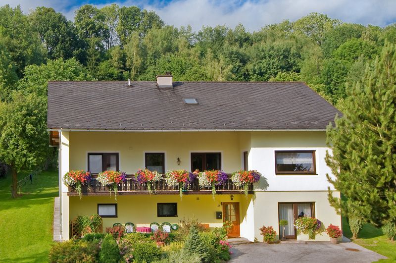 Zweistöckiges gelbes Haus mit Balkon und Blumen, umgeben von Bäumen und Garten.