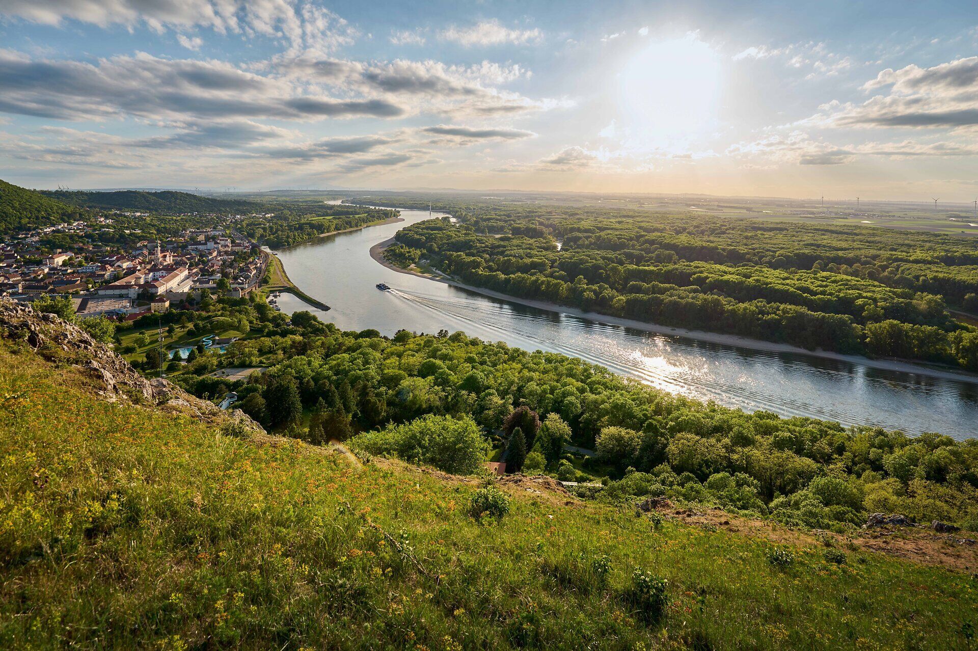 Blick vom Braunsberg auf Hainburg an der Donau, die Donauauen und ein Schiff auf dem Fluss im Abendlicht.