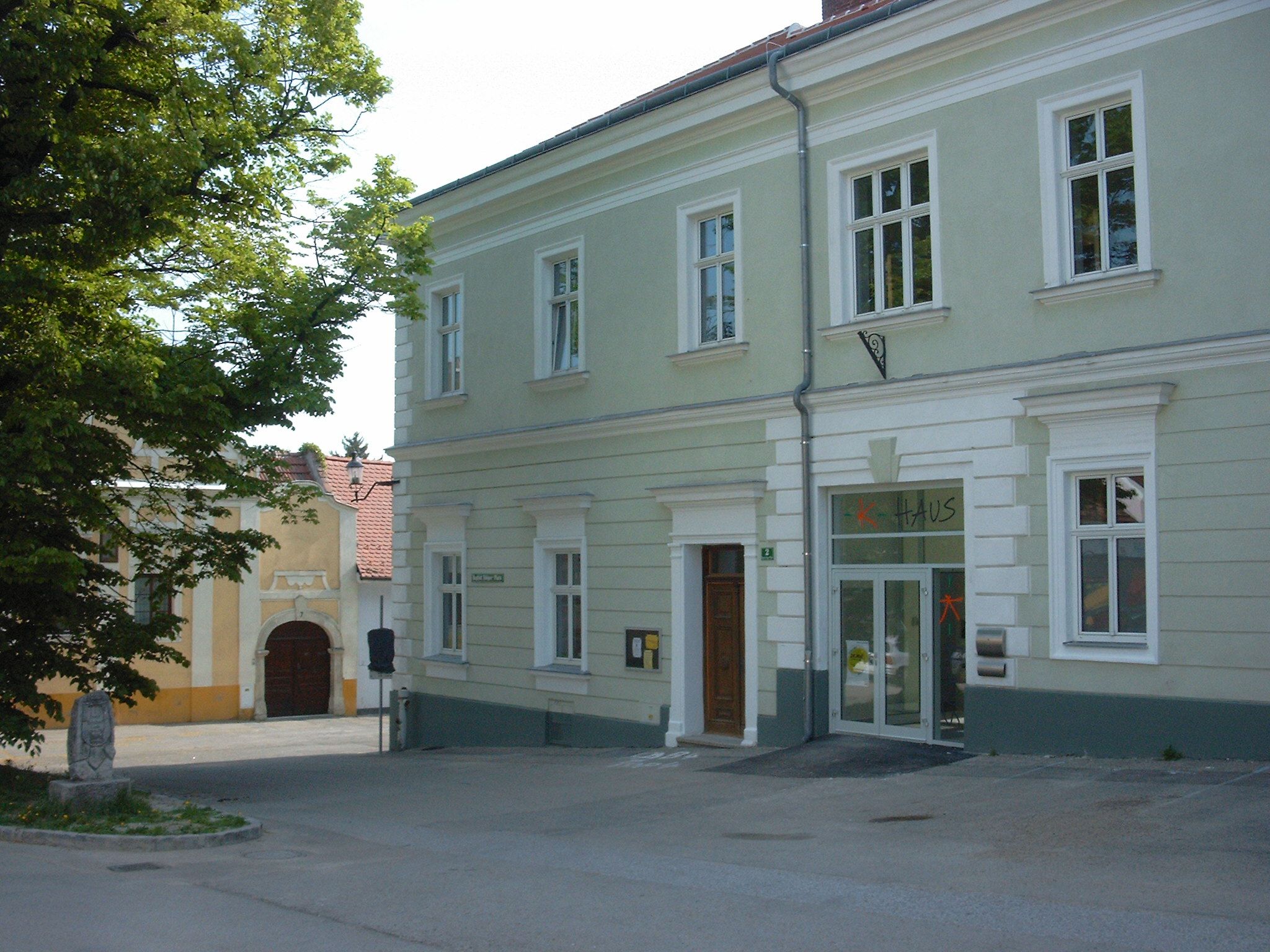 Ein zweistöckiges, hellgrünes Gebäude mit der Aufschrift 'Haus' über der Tür.