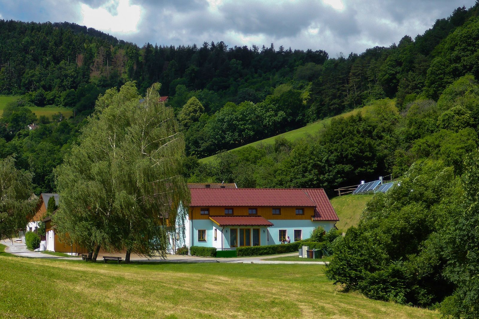 Ein Ferienhof mit roten Dächern in einer grünen, hügeligen Landschaft mit Bäumen und Wiesen.