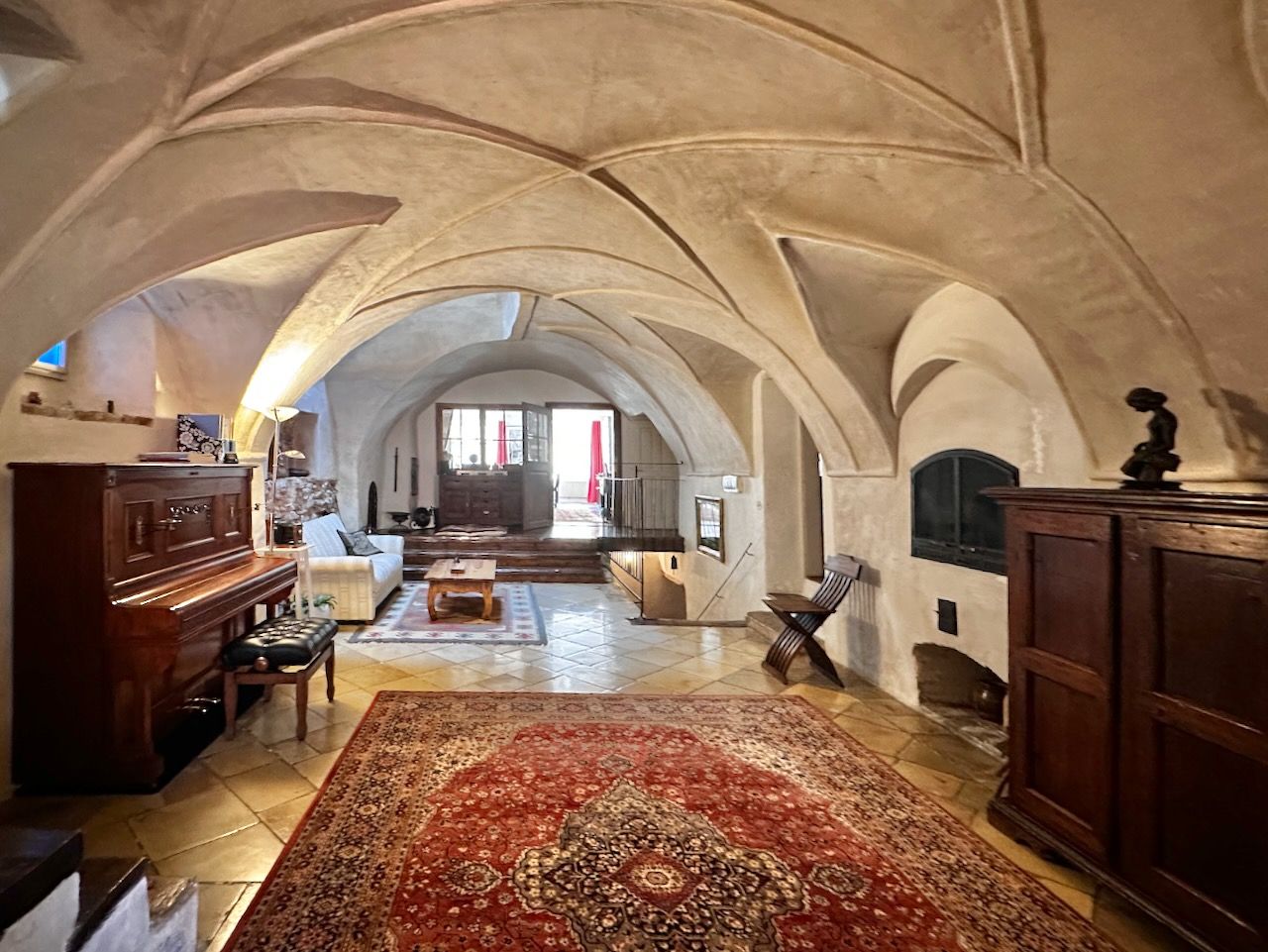 Historische Empfangshalle mit Gewölbedecke, Teppich, Klavier und Holzmöbeln.