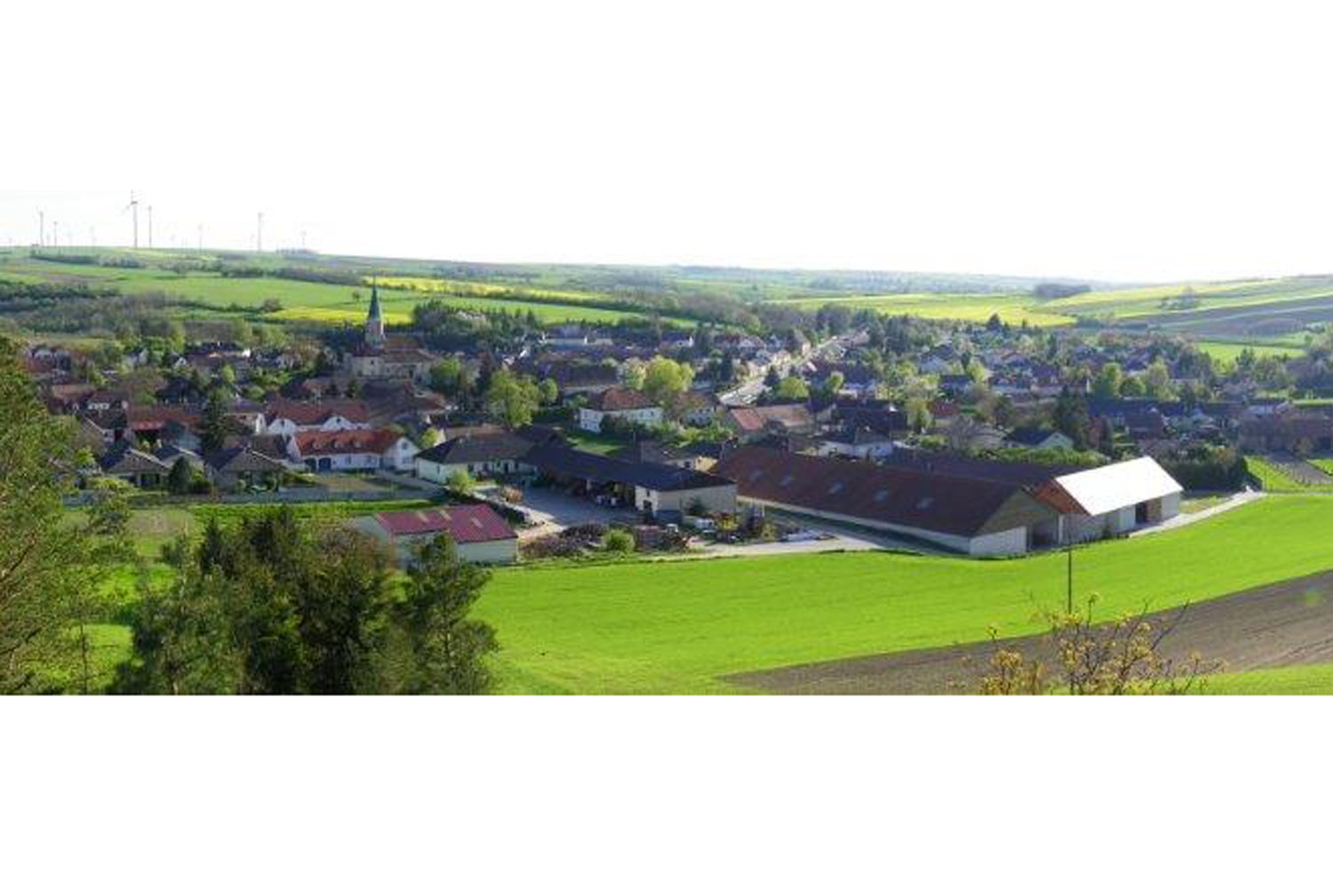 Landschaft mit Dorf und Kirche, umgeben von Feldern.