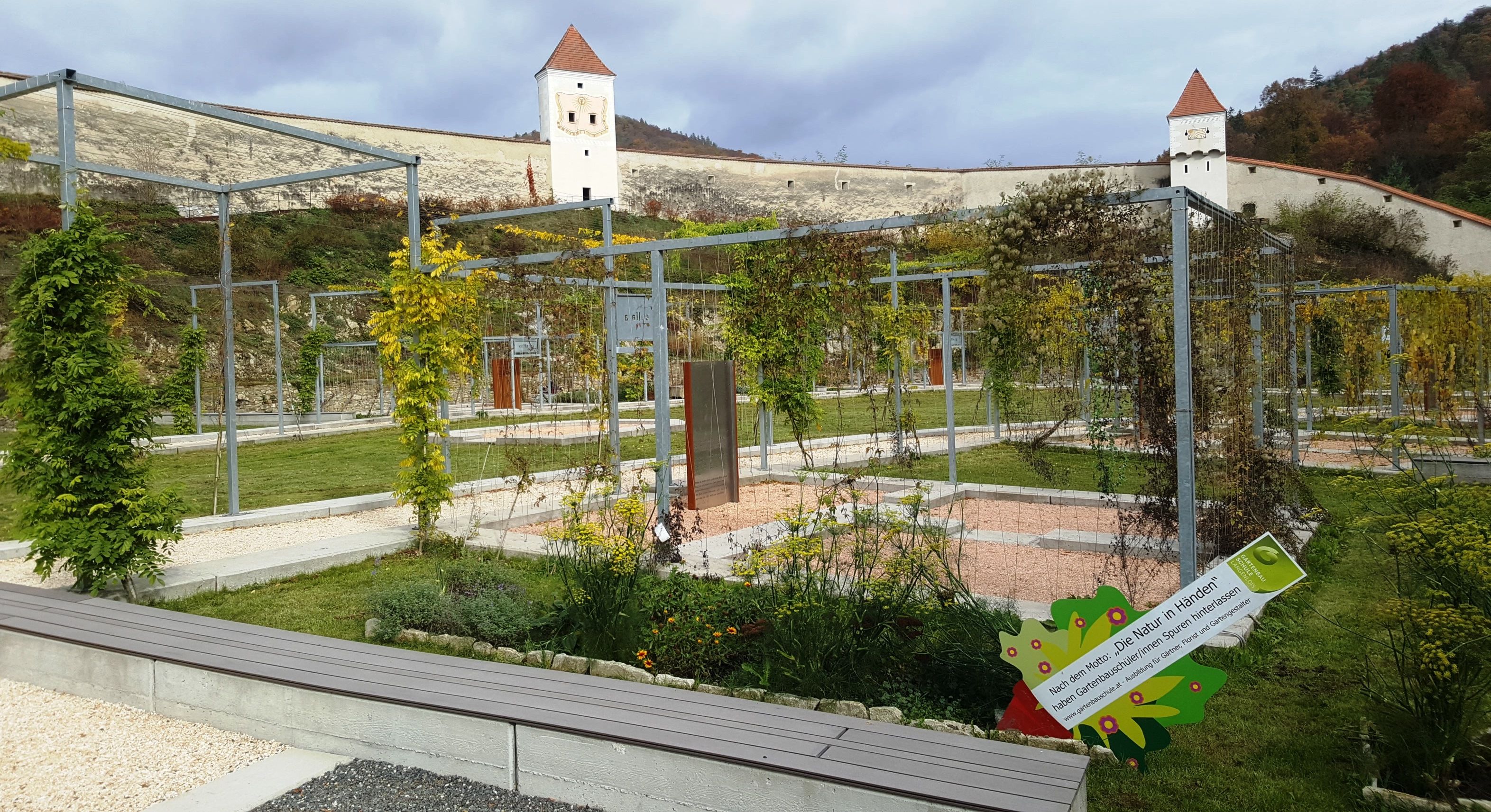 Gartenanlage der Kartause Aggsbach mit Metallstrukturen und Türmen im Hintergrund.