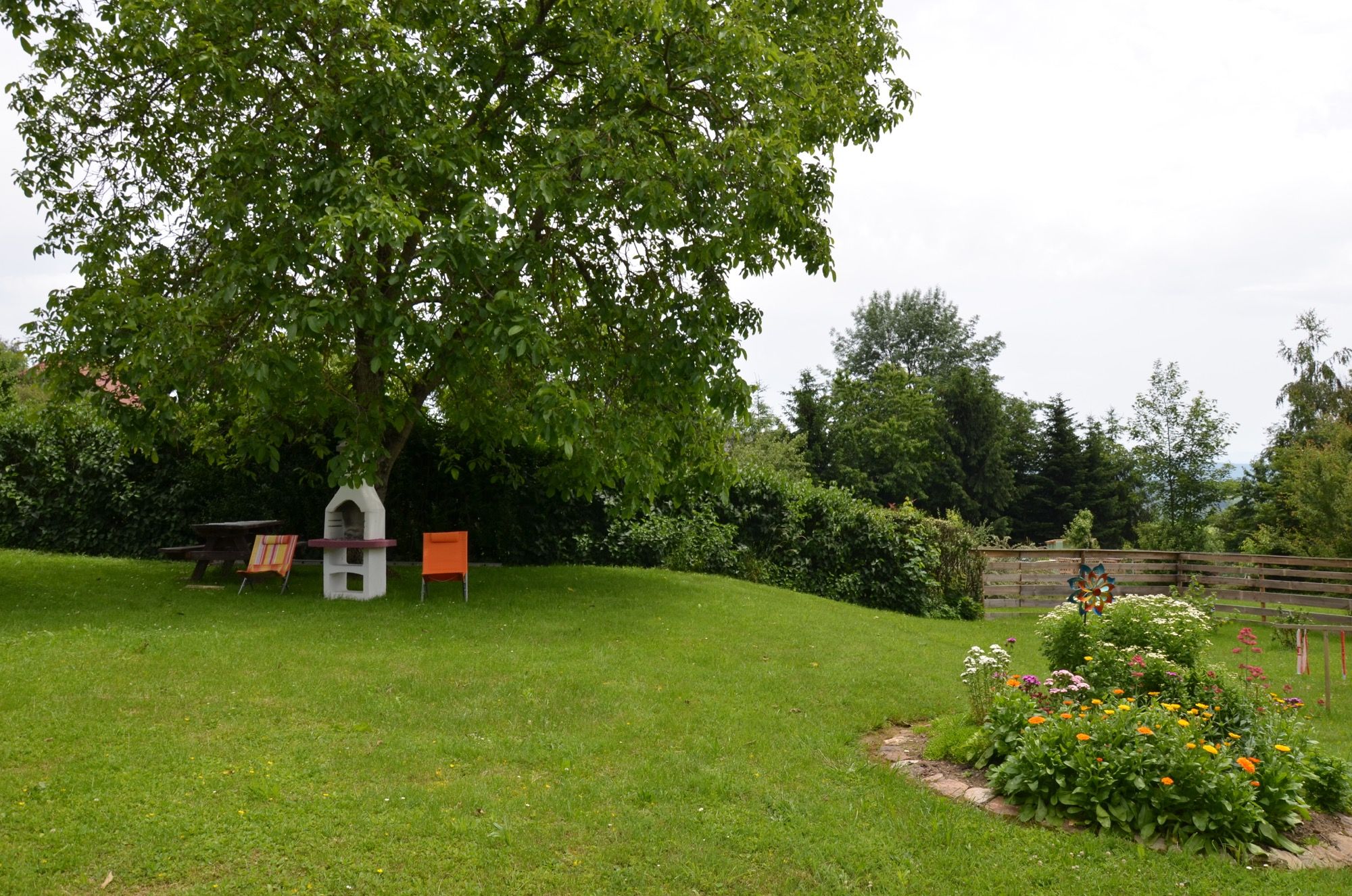 Ein grüner Garten mit einem Baum, Gartenmöbeln und Blumenbeet.