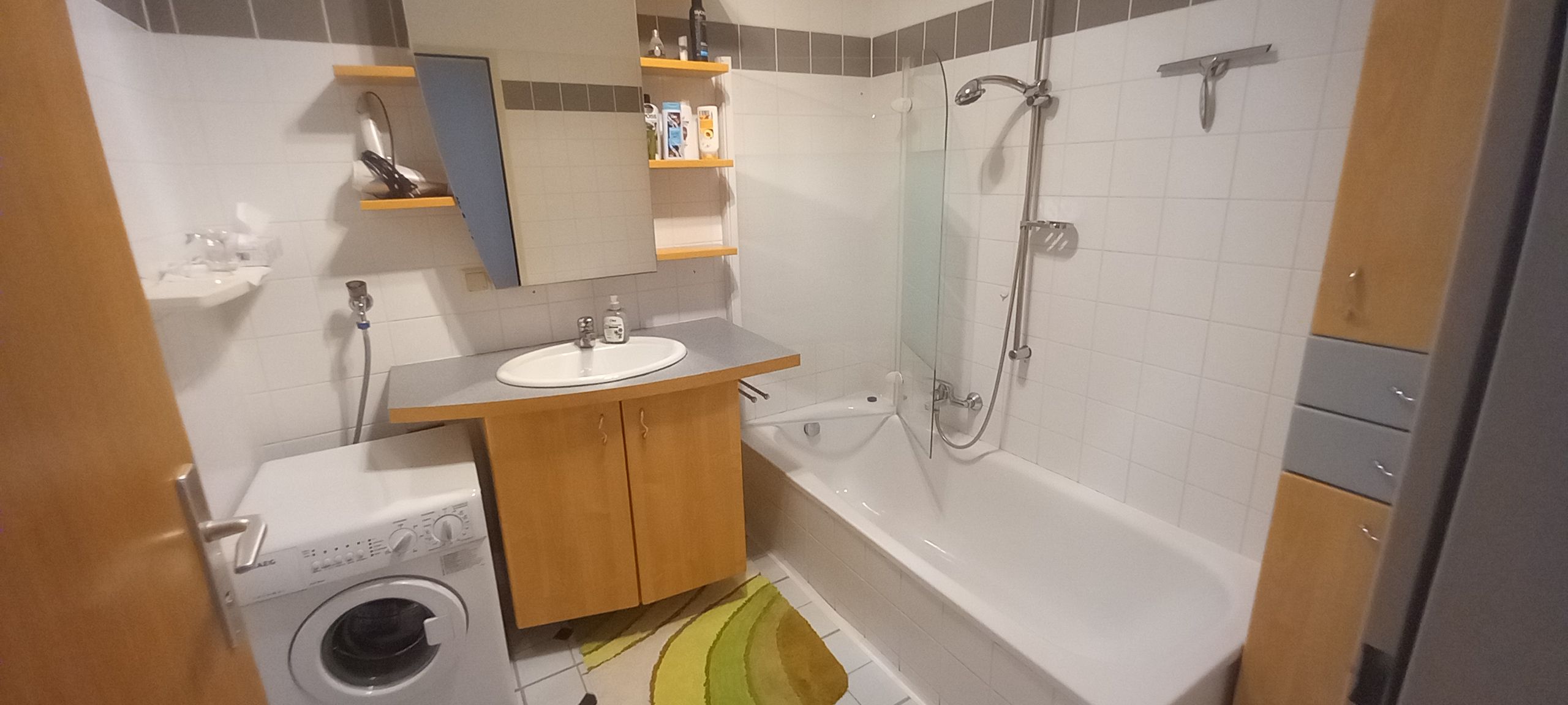 Modernes Badezimmer mit Waschmaschine, Waschbecken, Badewanne und Regalen.