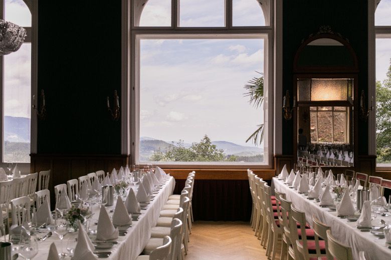 Eleganter Speisesaal mit gedeckten Tischen und Blick auf die Berge durch ein großes Fenster.