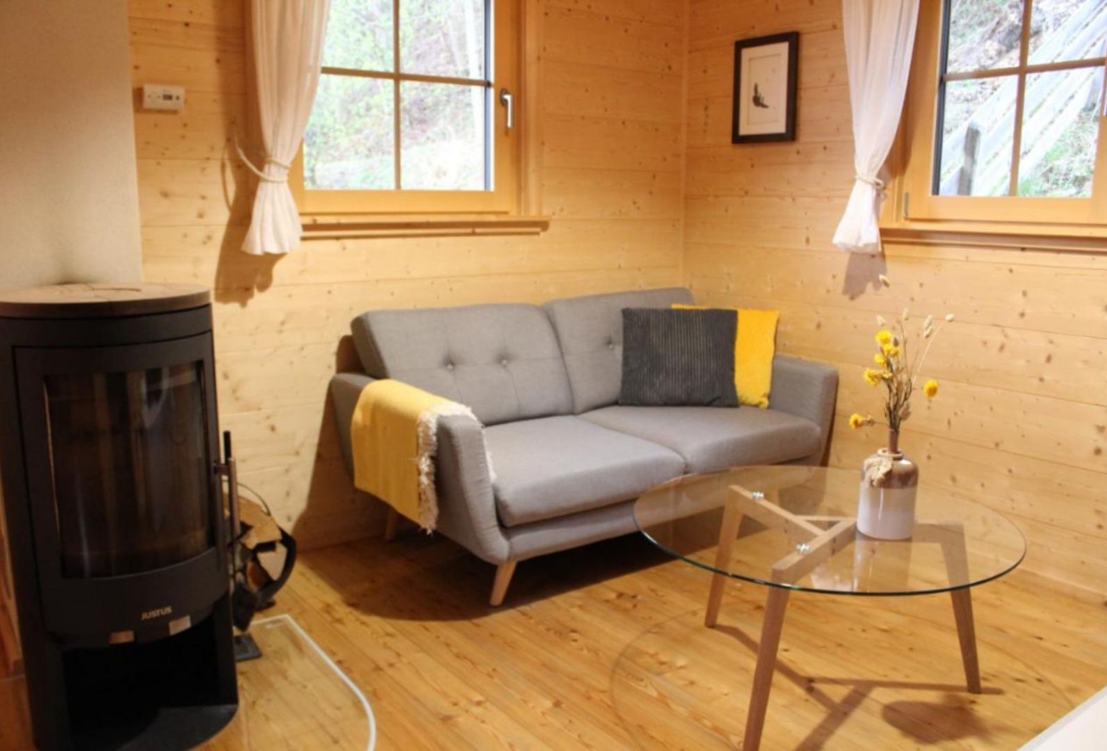 Gemütliches Wohnzimmer mit grauem Sofa, Holzwänden, Kamin und Glastisch.