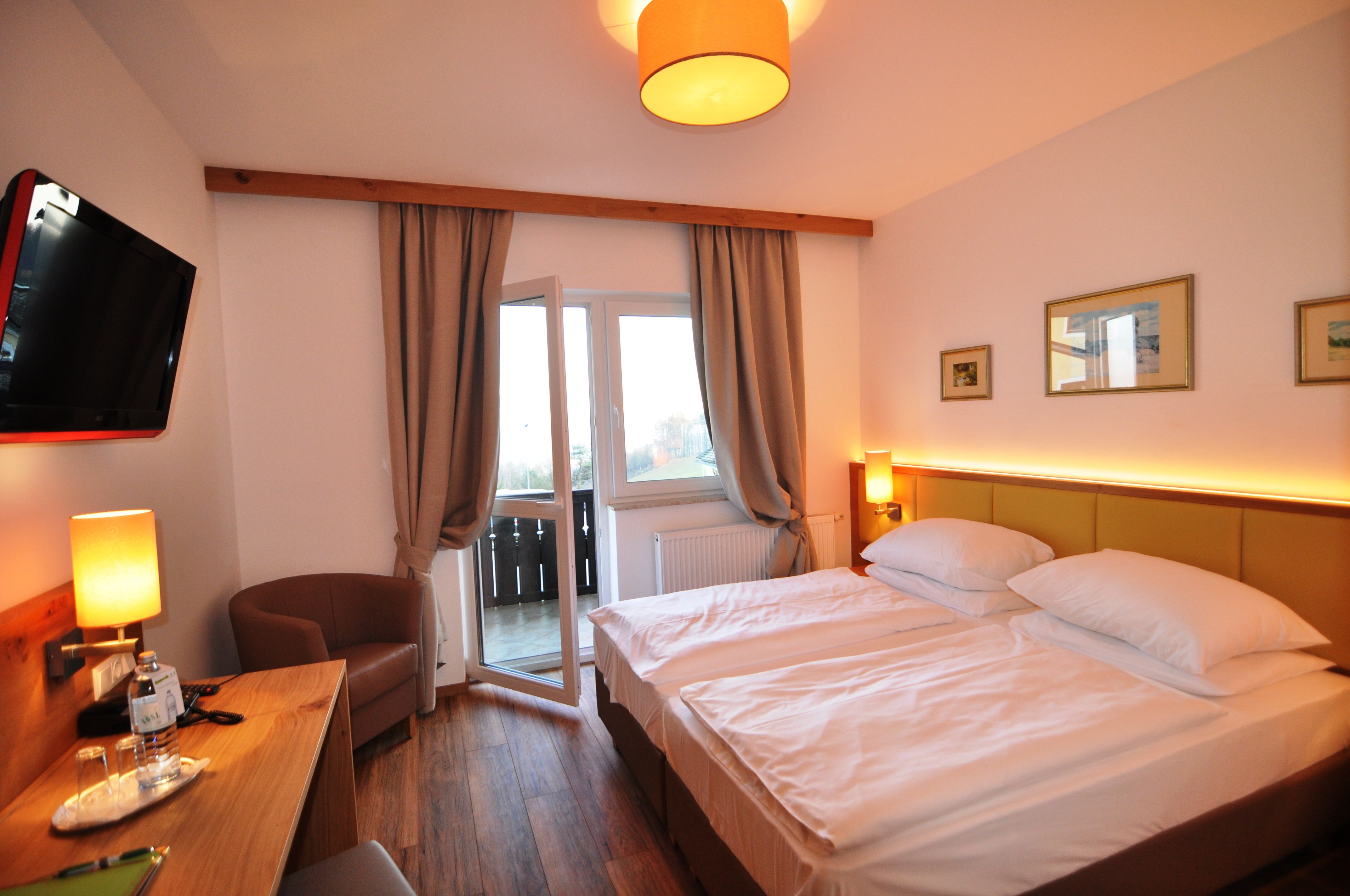 Hotelzimmer mit Doppelbett, Fernseher, Schreibtisch und offenem Balkonfenster.