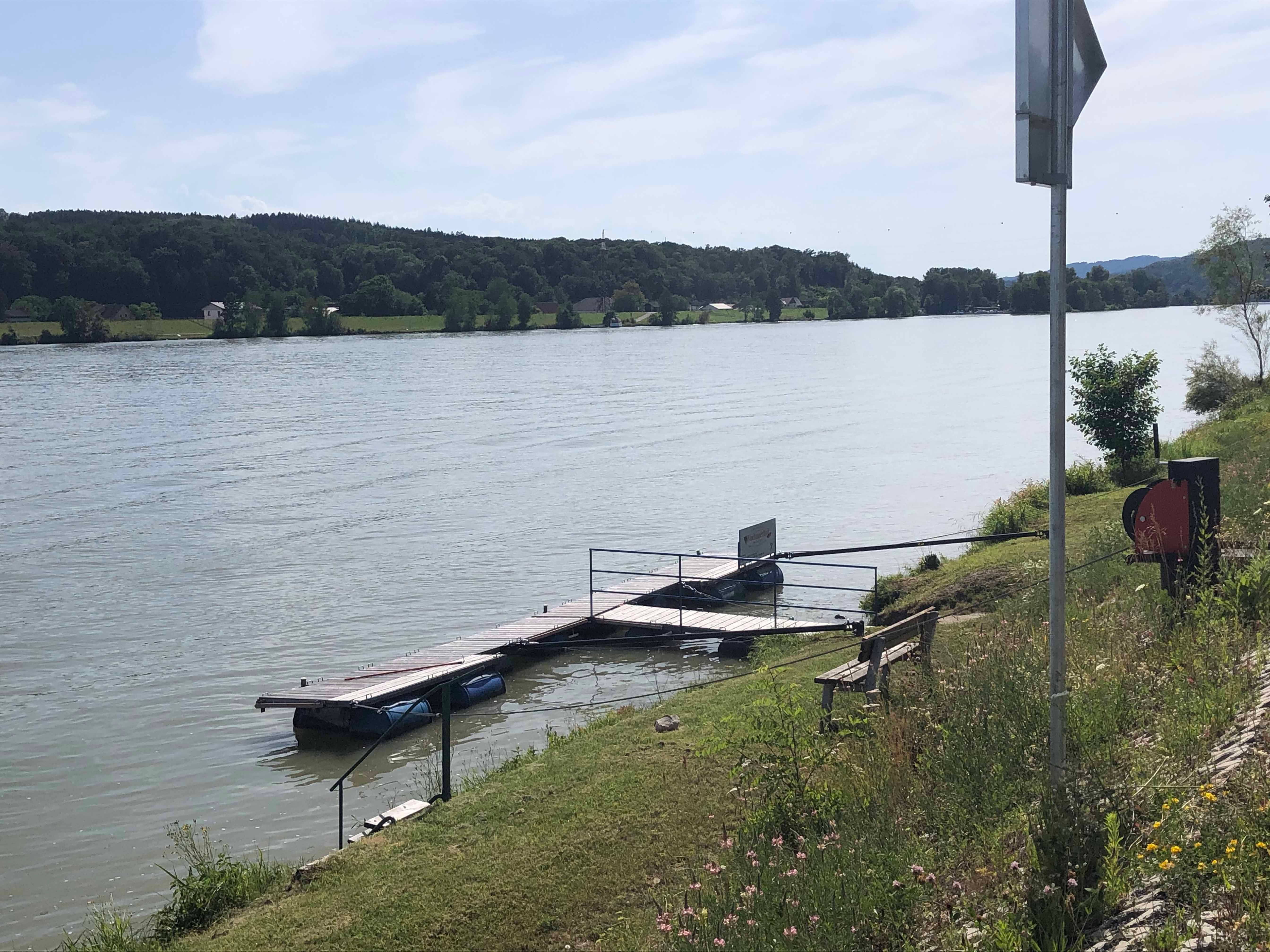 Anlegesteg am Flussufer mit Bank und Vegetation.