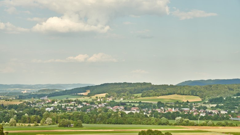 Landschaft mit Feldern, H&uuml;geln und einem Dorf im Hintergrund unter einem bew&ouml;lkten Himmel.